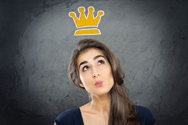 A woman pouting with her head tilted back, a yellow crown floating above her head on a dark grey background, © lassedesignen/Adobe Stock