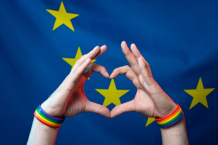 Men's hands with bracelets with LGBT symbols folded a heart from their fingers against the background of the European Union flag