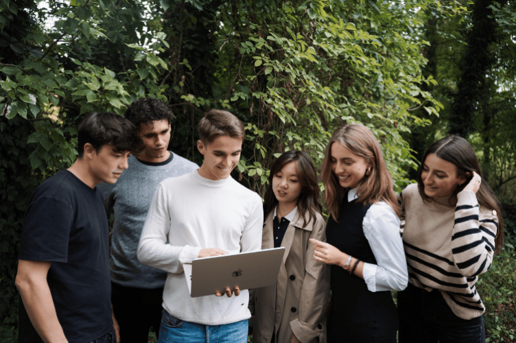 A group of students standing in the woods looking at a laptop for the ESCP webinar