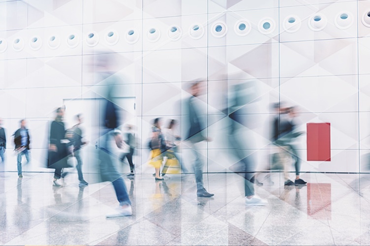 Une foule floutée marche dans un grand hall blanc et moderne