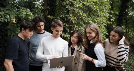 A group of students standing in the woods looking at a laptop for the ESCP webinar