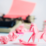 Pink,Origami,Unicorn,With,Crumpled,Paper,Balls,And,A,Typewriter.