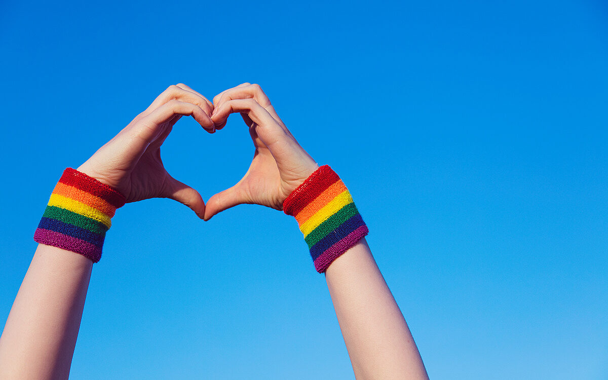 AdobeStock – ink drop Hand making a heart sign with gay pride LGBT rainbow flag wristband