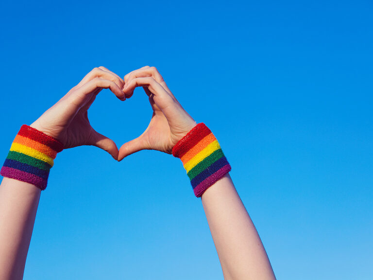 Hand making a heart sign with gay pride LGBT rainbow flag wristband