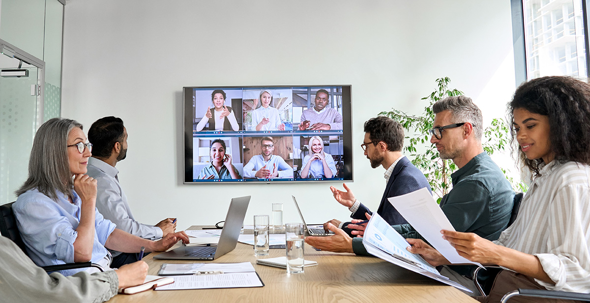 Diverse company employees having online business conference video call on tv screen monitor in board meeting room.