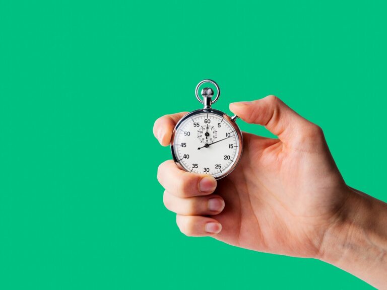 A hand holds a stopwatch in front of a bright green background