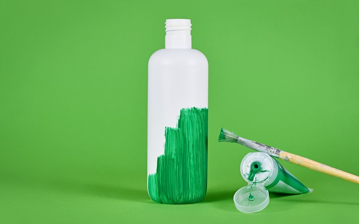 ©Firn / Adobe Stock Photo of a white bottle on a green background, half painted by green paint with the paintbrush and open paint next to it.