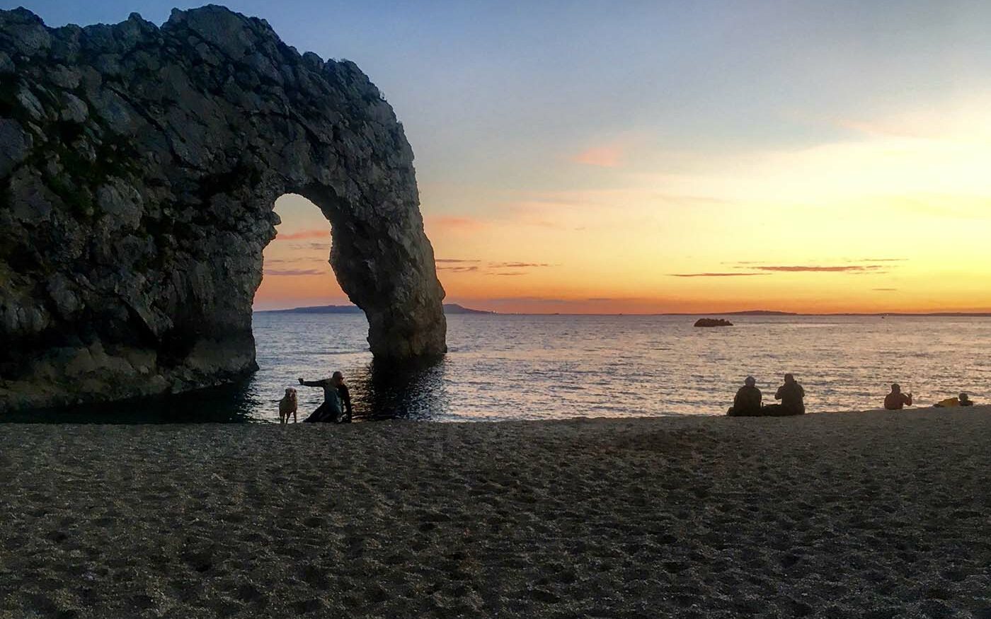 ©AdventureUncovered Photo of a beach at sunset with some people and a dog enjoying the view.