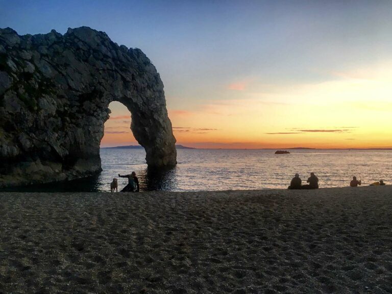Photo of a beach at sunset with some people and a dog enjoying the view.