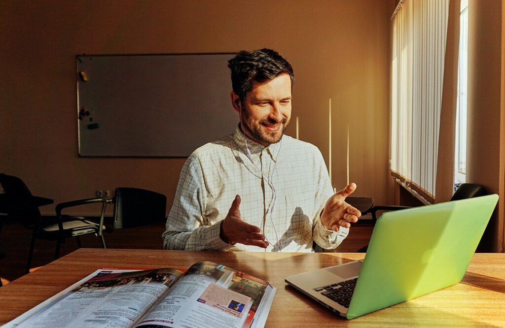 Photo of a man looking at a computer with his hands in the air indicating that he is talking.