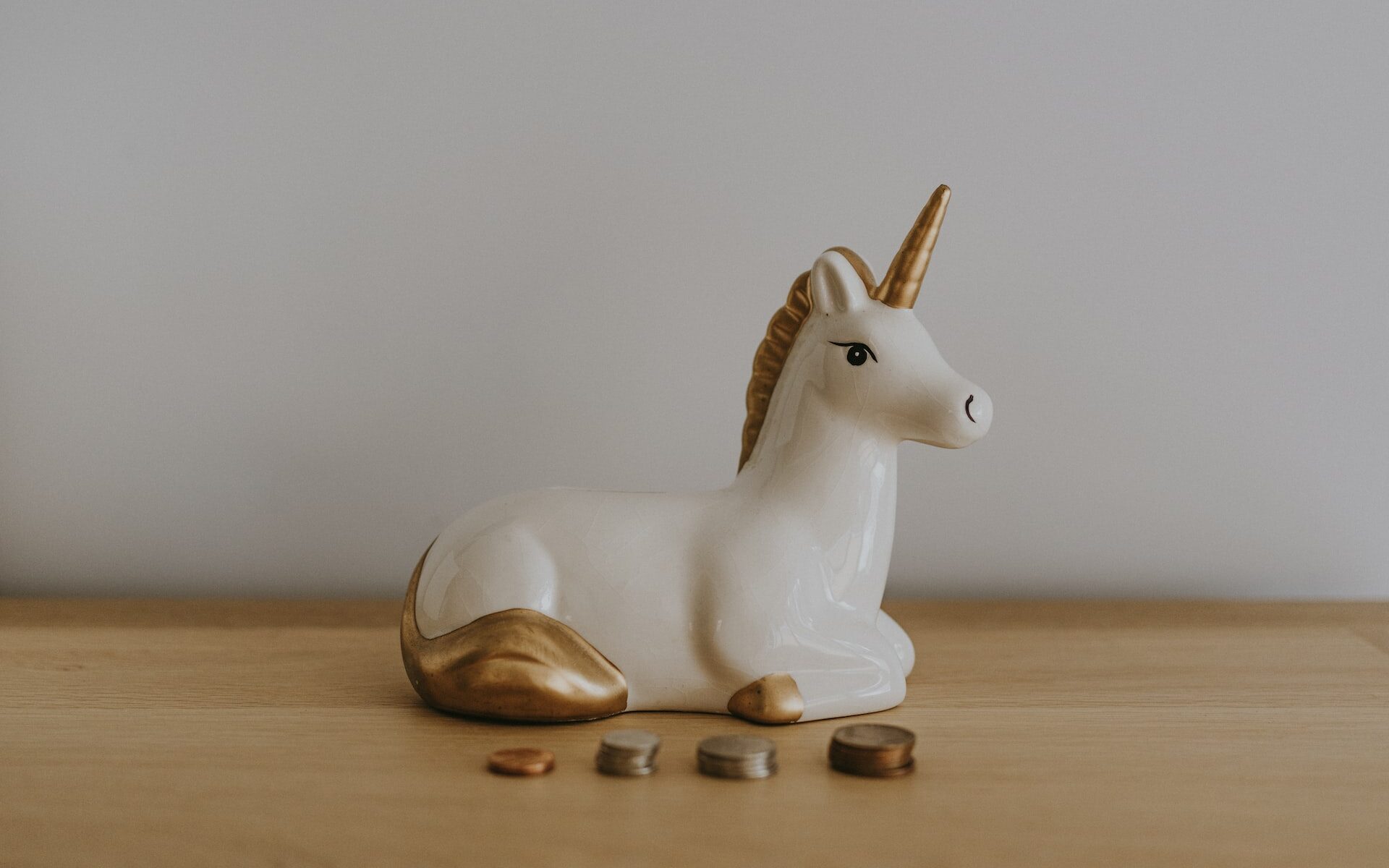 ©Annie Spratt/Unsplash A ceramic unicorn sitting on a desk in front of stacks of coins.