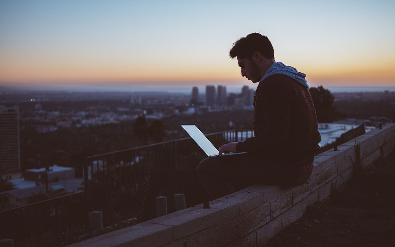 © Avi Richards/Unsplash A man sitting on a concrete brick with an open laptop on his lap. © Avi Richards / Unsplash