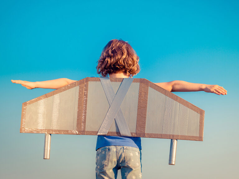 A child wearing wings made out of cardboard and duct tape ready to fly into the bright blue sky