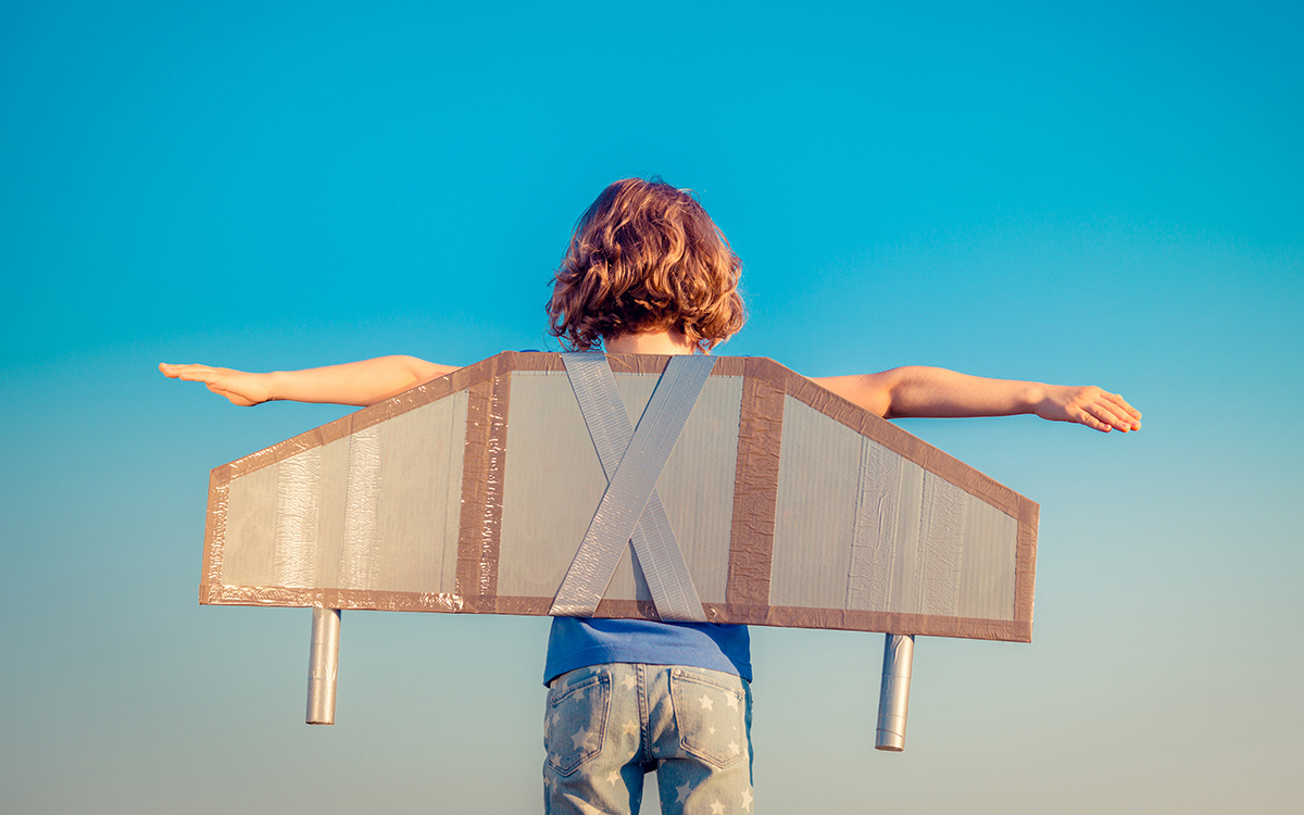 A child wearing wings made out of cardboard and duct tape ready to fly into the bright blue sky