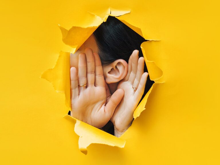 Photo of a woman holding her ear like she is listening closely