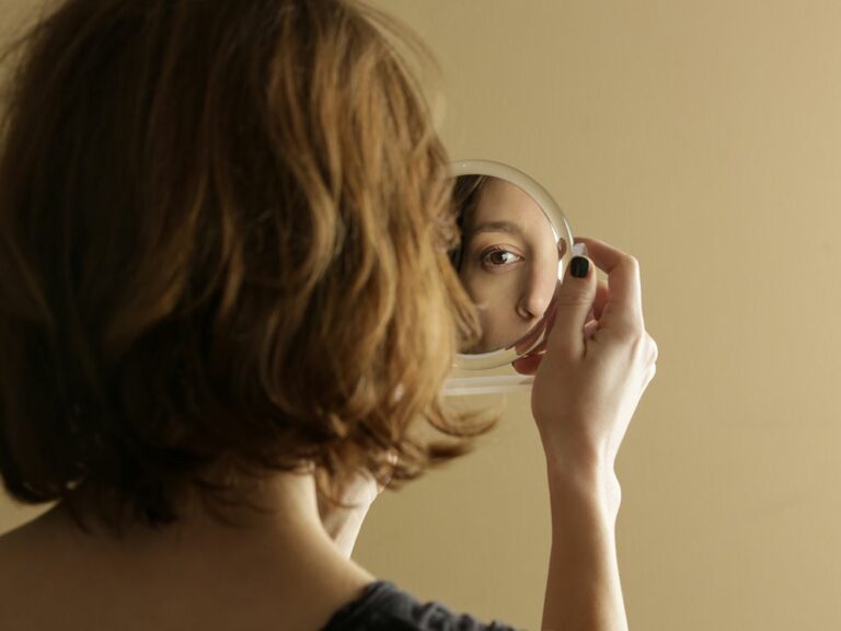 Photo of a girl with her back turned to the camera looking into a mirror.