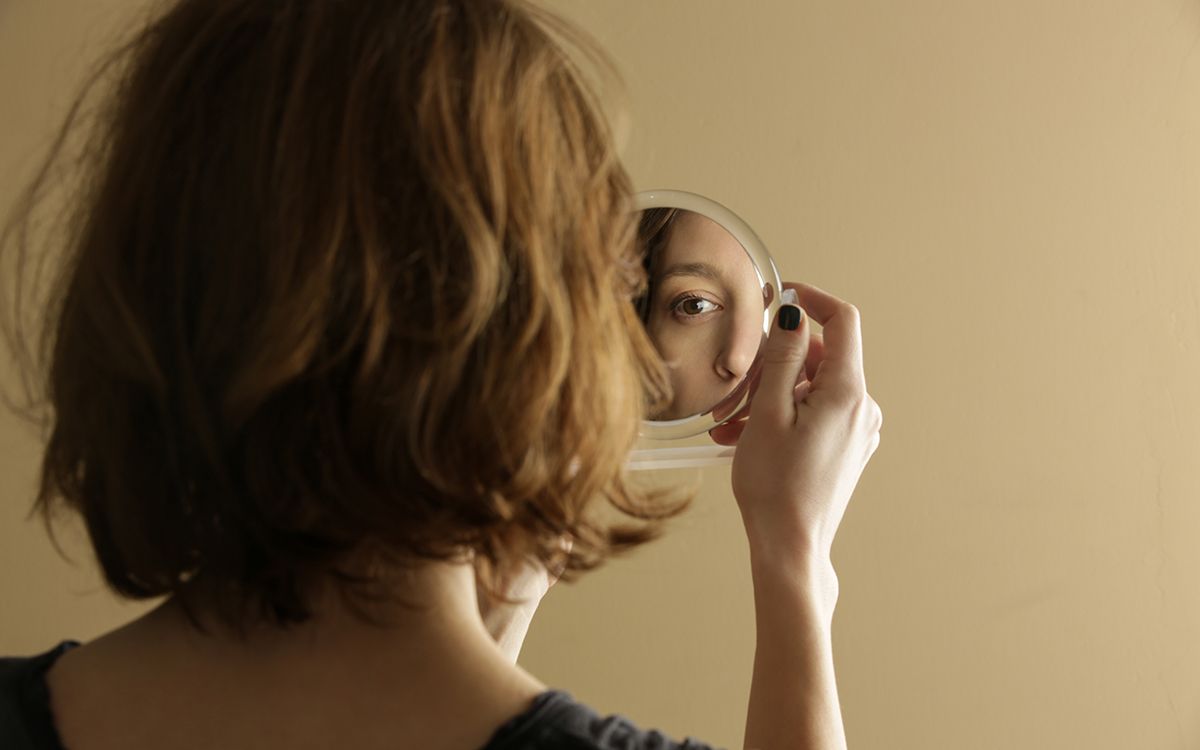 Photo of a girl with her back turned to the camera looking into a mirror.