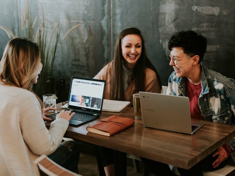 Picture of three young women sitting around a table, talking and laughing.