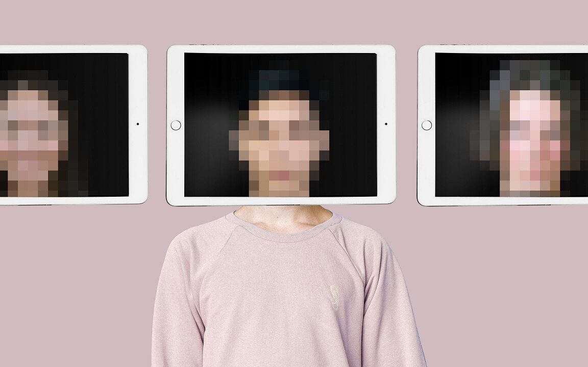©Collagery / Shutterstock A person stands in front of a pink wall. An iPad is being held in front of their face and the image of their face is distorted, so you can't be sure who you're seeing.