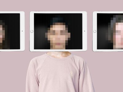 A person stands in front of a pink wall. An iPad is being held in front of their face and the image of their face is distorted, so you can't be sure who you're seeing.