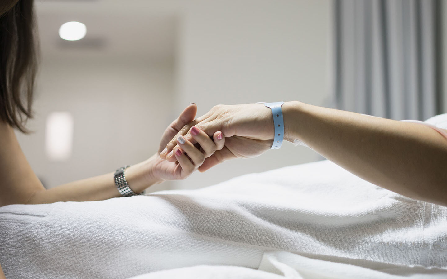 Photo-Credit-bozzybozza-adobe-stock hand of man and woman couple in hospital and patient bed with hospital tag on wrist with love hope and care