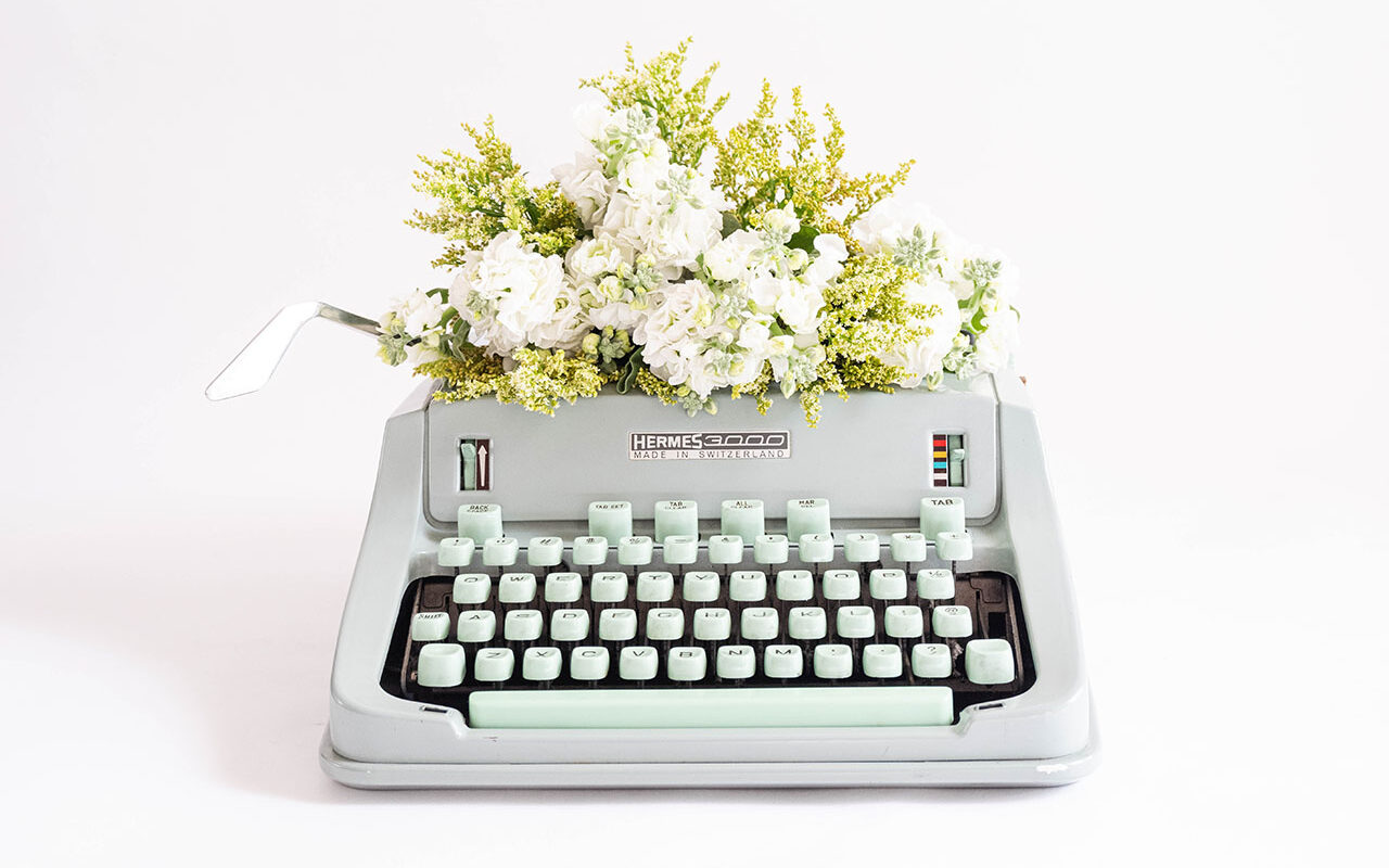 © Fiona Murray / Unsplash A typewriter with white florals and greenery, © Fiona Murray / Unsplash