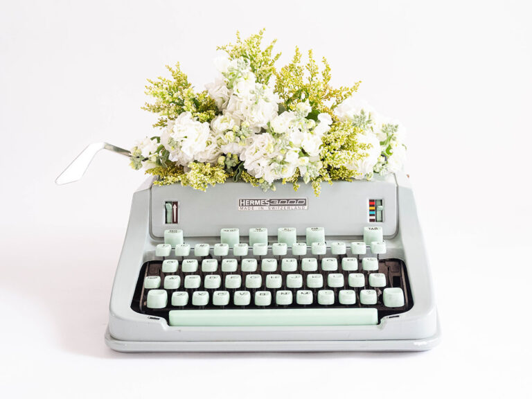 A typewriter with white florals and greenery, © Fiona Murray / Unsplash