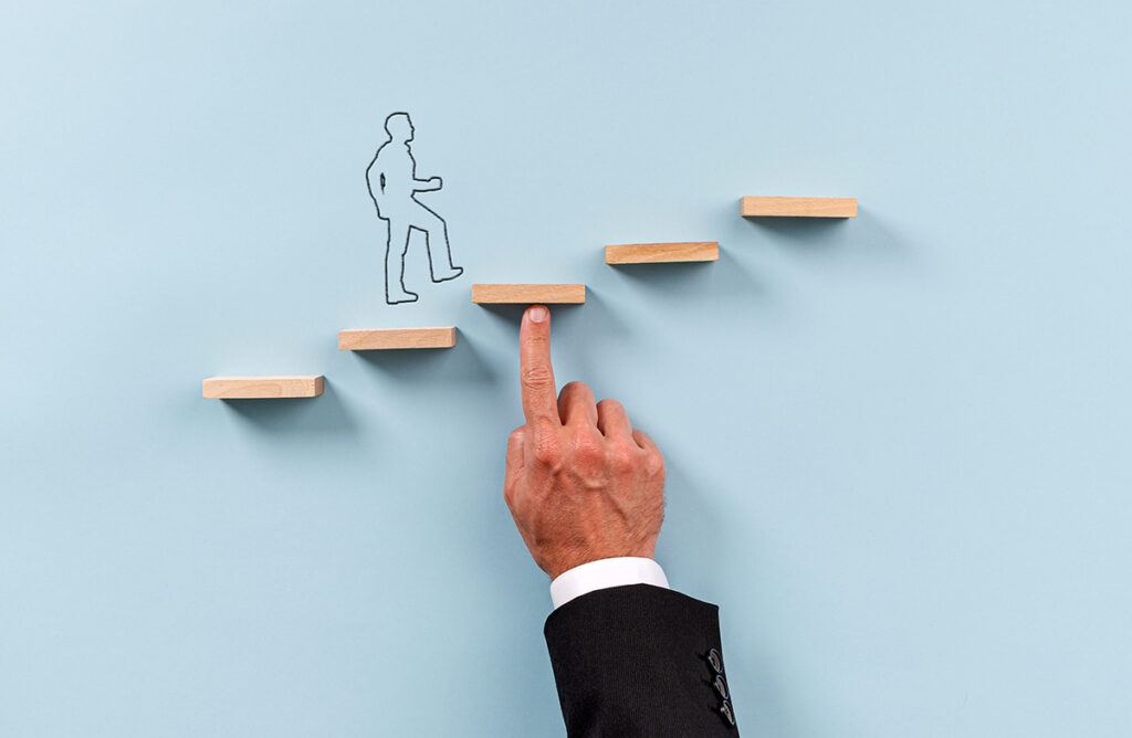 Hand of a businessman supporting wooden step for a silhouetted man to walk upwards