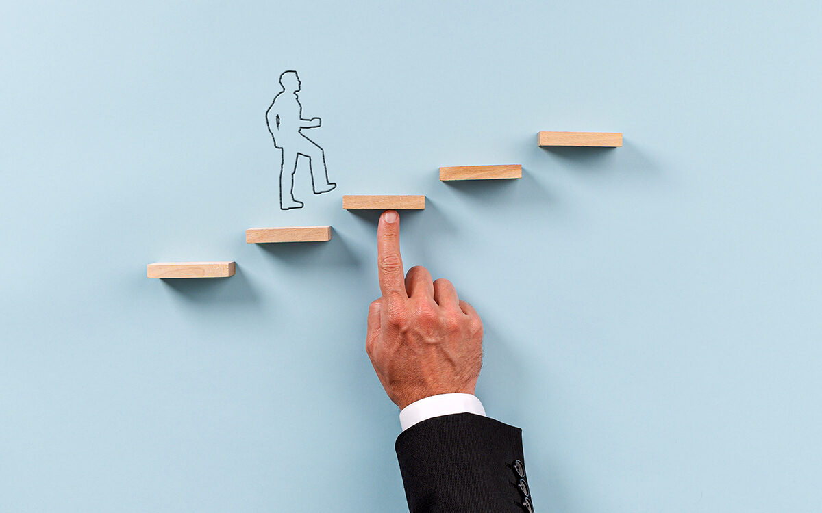 Gajus-AdobeStock Hand of a businessman supporting wooden step for a silhouetted man to walk upwards