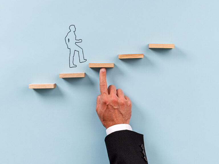 Hand of a businessman supporting wooden step for a silhouetted man to walk upwards