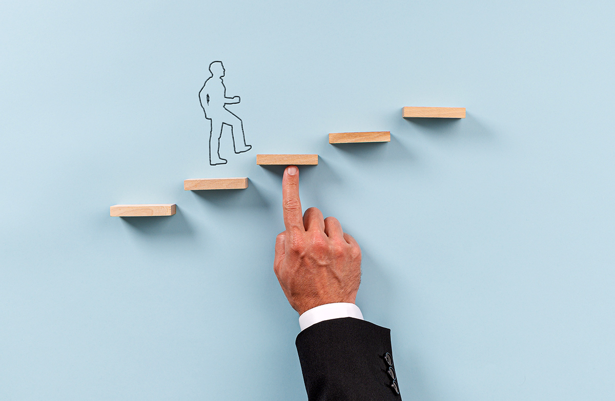 Hand of a businessman supporting wooden step for a silhouetted man to walk upwards