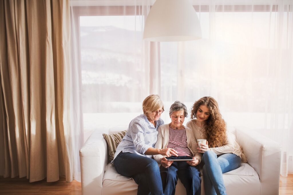 A teenage girl and mother teaching the grandmother how to use a tablet.