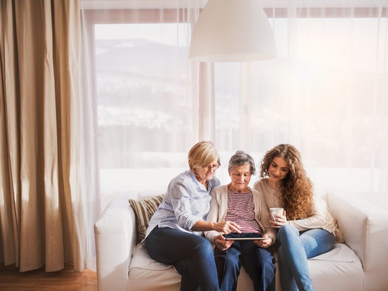 A teenage girl and mother teaching the grandmother how to use a tablet.