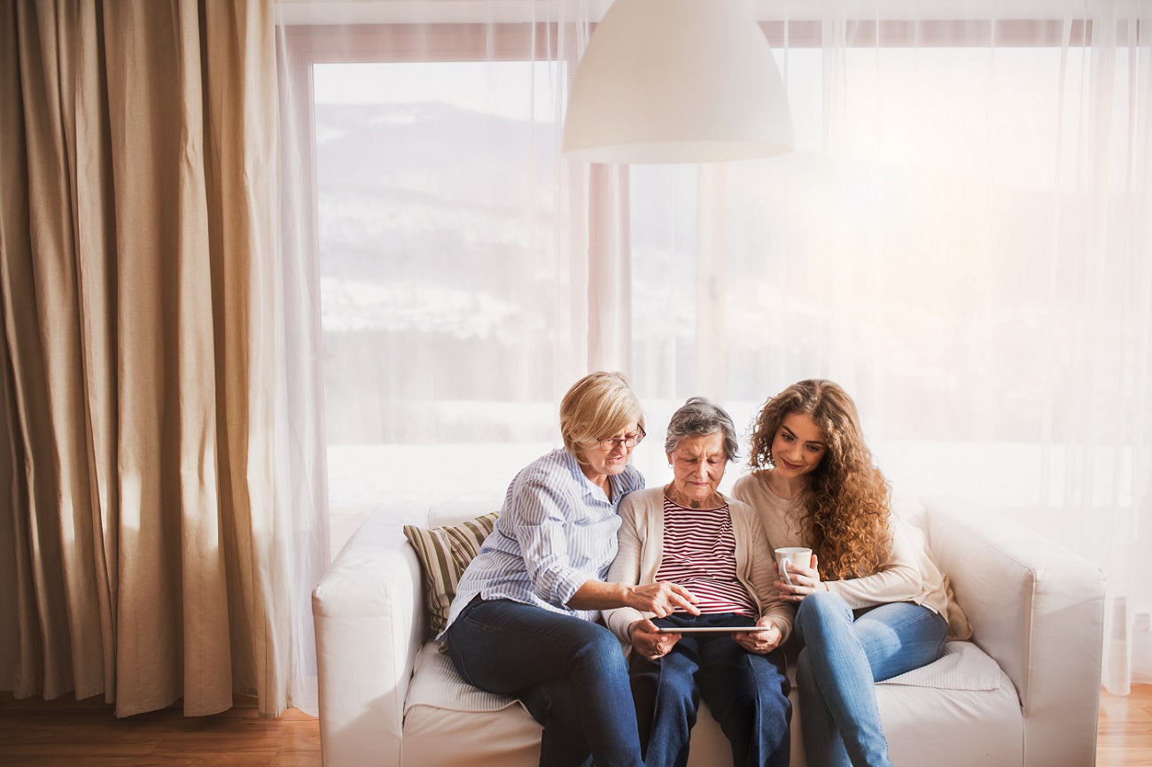A teenage girl and mother teaching the grandmother how to use a tablet.