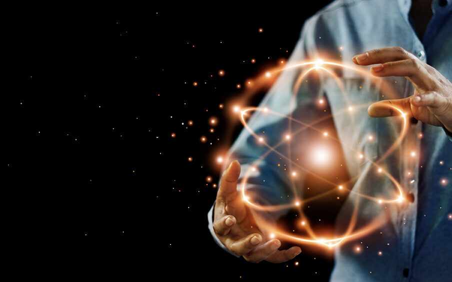 ipopba/AdobeStock Abstract science, hands holding atomic particle, nuclear energy imagery and network connection on dark background.