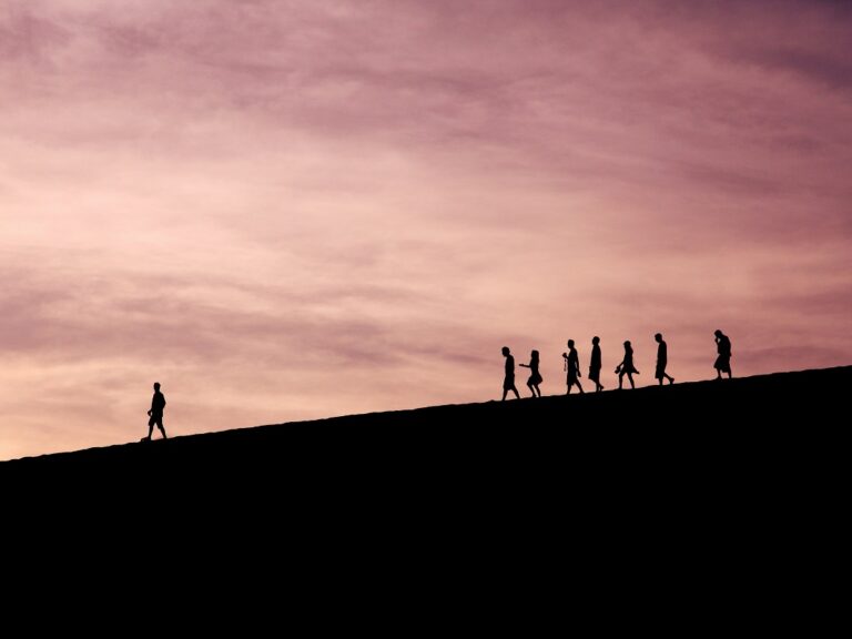 Silhouettes of people walking along the top of a hill. One person is out in front, leading the way.