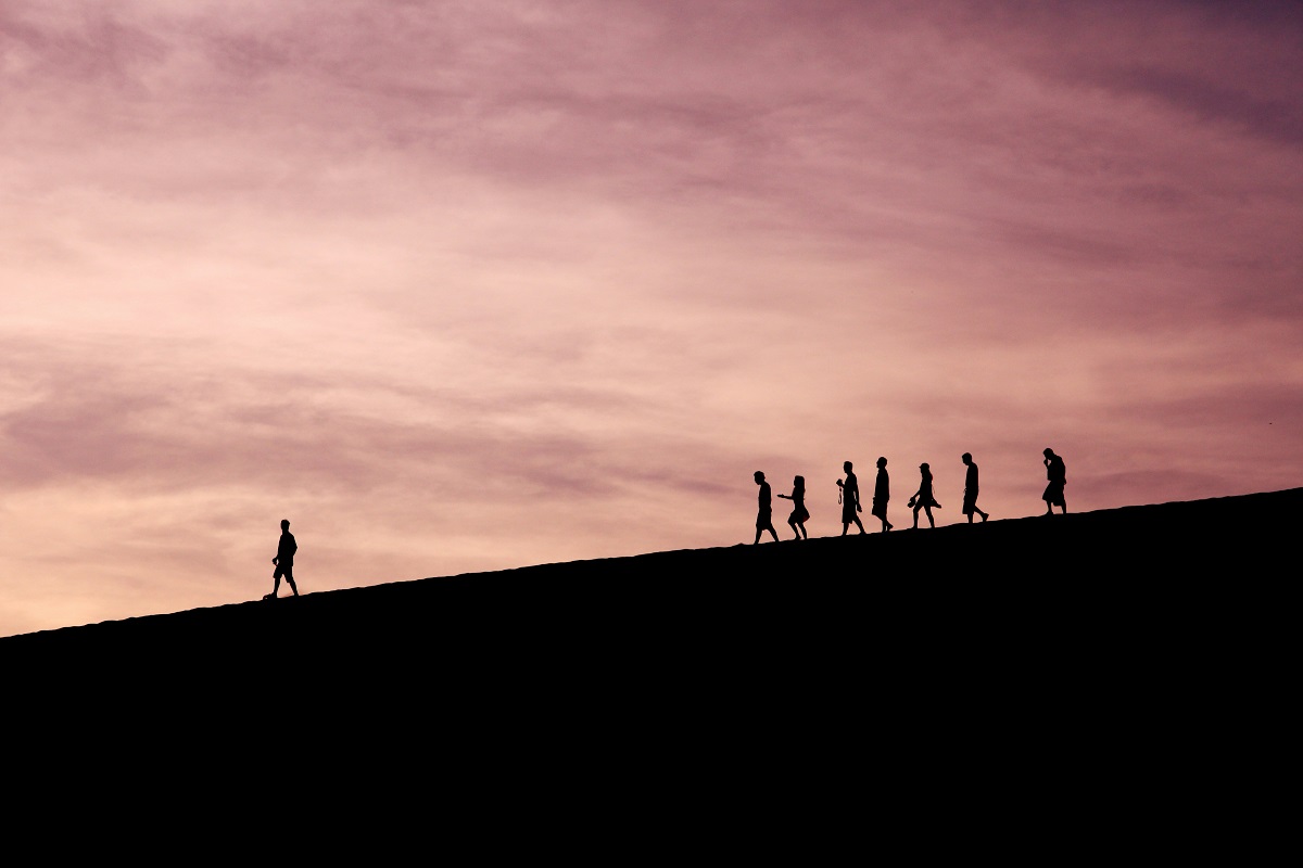 Silhouettes of people walking along the top of a hill. One person is out in front, leading the way.