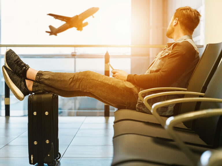 Man sitting on gang chair with feet on luggage looking at airplane,