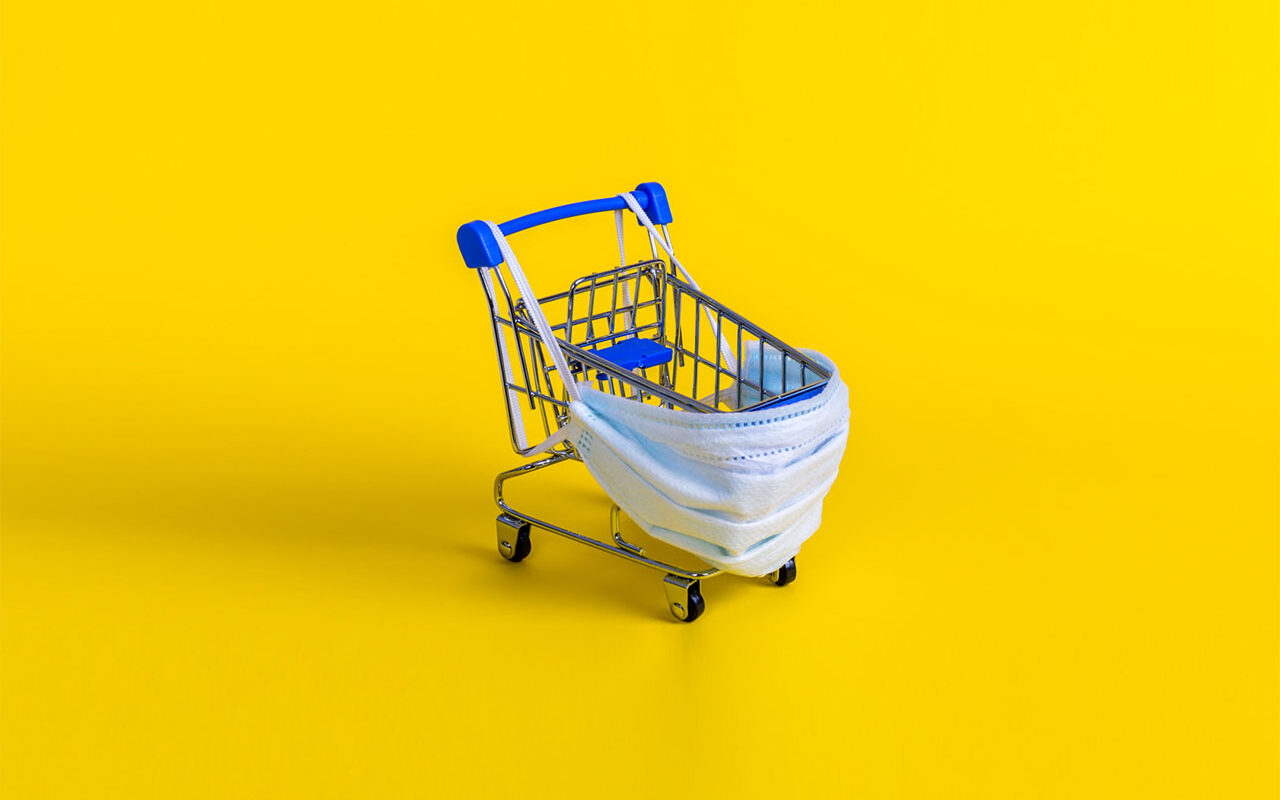 Julia-Lavrinenko-AdobeStock Blue shopping cart with medical mask for virus protection on yellow background.
