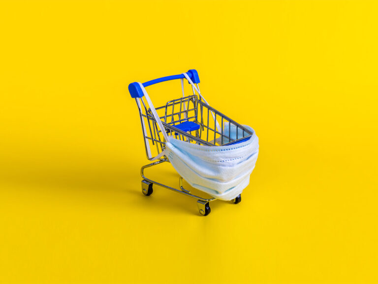 Julia-Lavrinenko-AdobeStock Blue shopping cart with medical mask for virus protection on yellow background.