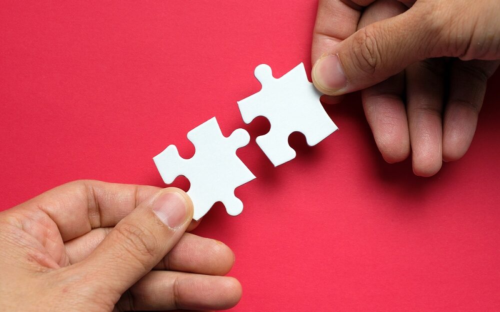 ©Kenishirotie/Adobestock Partnership concept with hands putting puzzle pieces together on red background