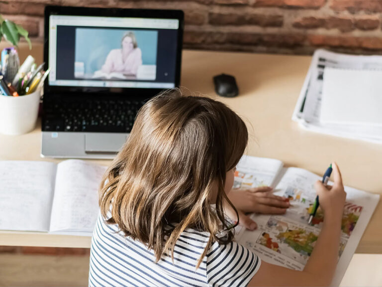 The concept of distance online learning self-isolation. Child sitting home desk doing lessons through a digital laptop.