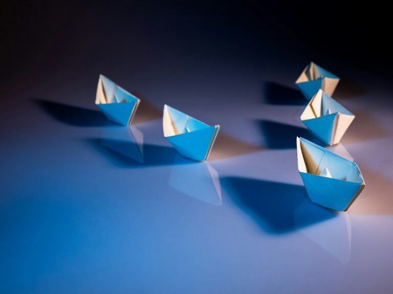 Five paper boats in a v formation, following one at the front