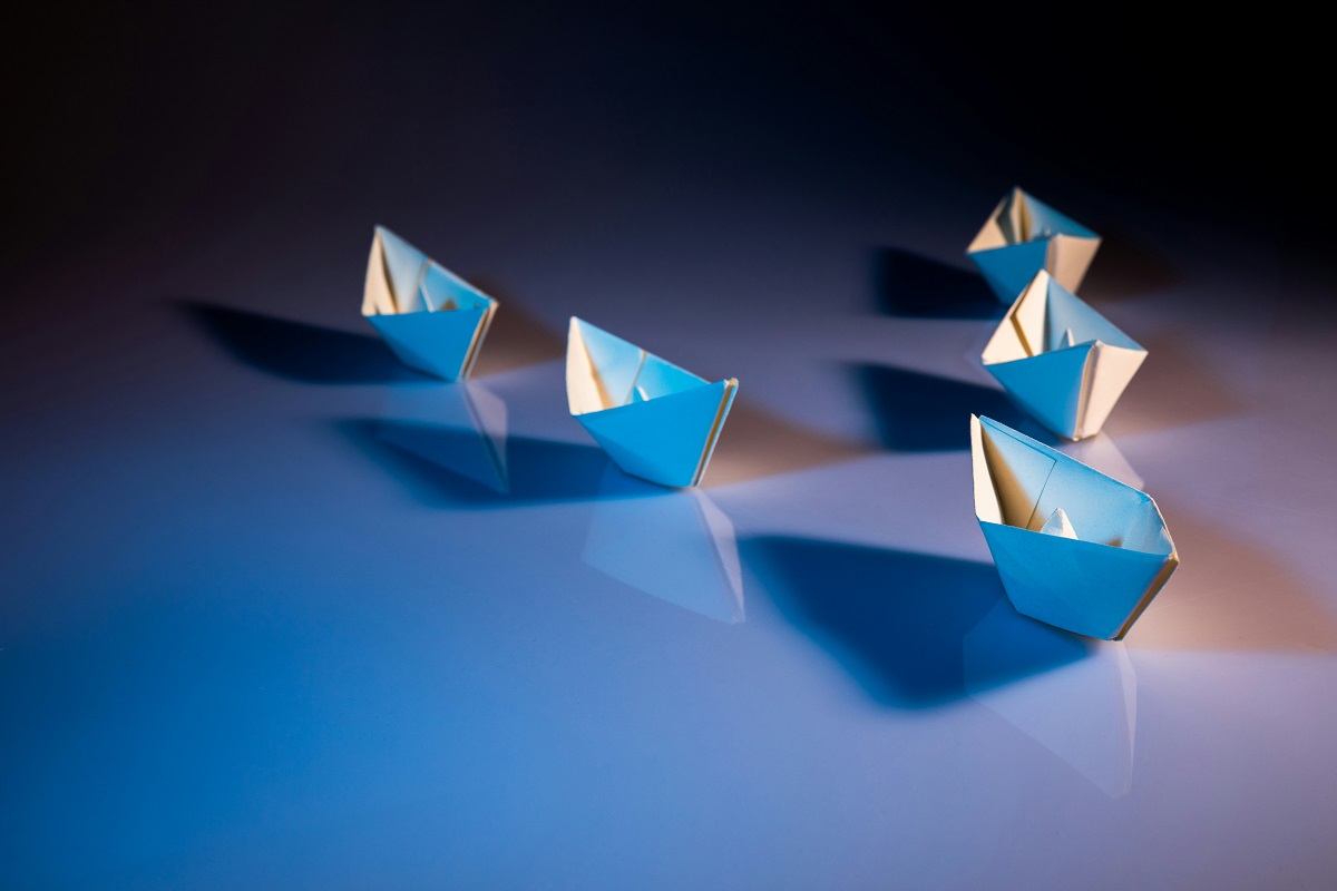 Five paper boats in a v formation, following one at the front