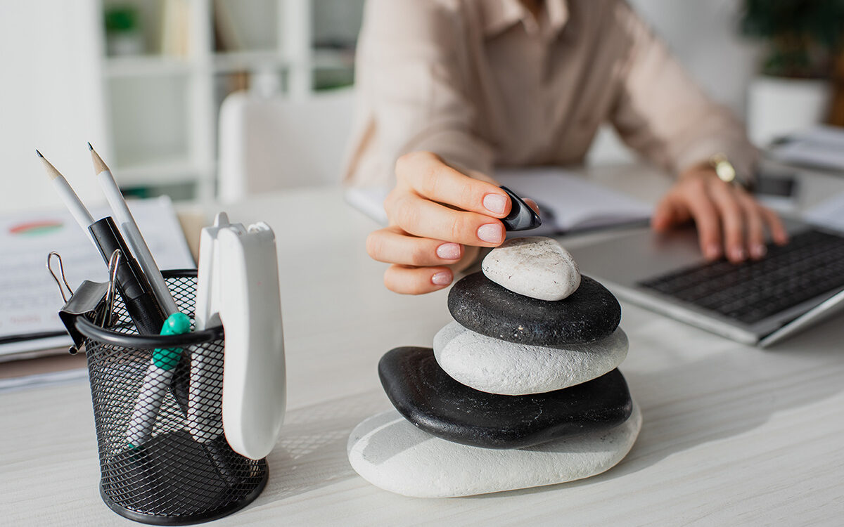 LIGHTFIELD STUDIOS – AdobeStock Cropped view of businesswoman working with laptop at workplace with zen stones.