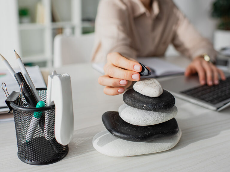 Cropped view of businesswoman working with laptop at workplace with zen stones.