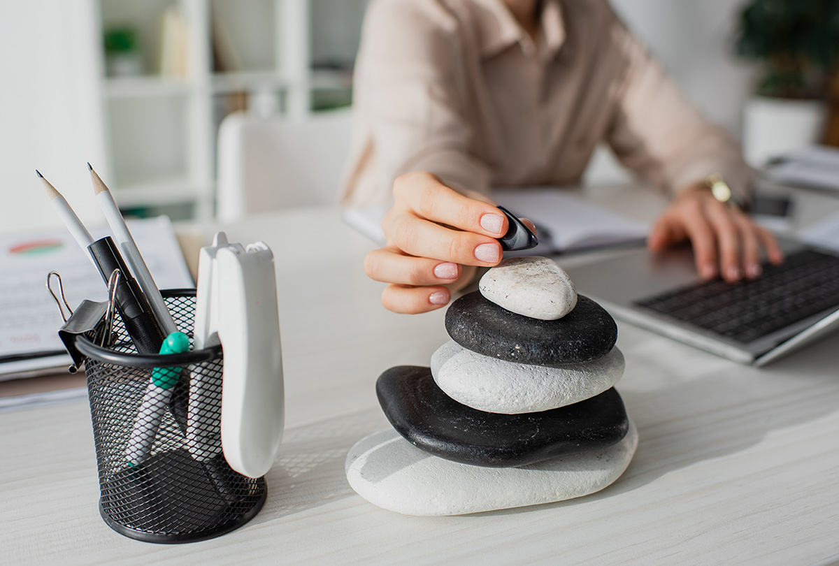 Cropped view of businesswoman working with laptop at workplace with zen stones.