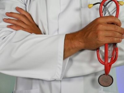A doctor stands with his arms crossed holding a stethoscope. We do not see his face.
