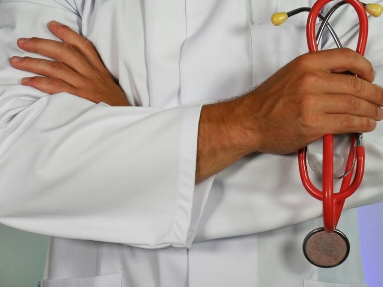 A doctor stands with his arms crossed holding a stethoscope. We do not see his face.