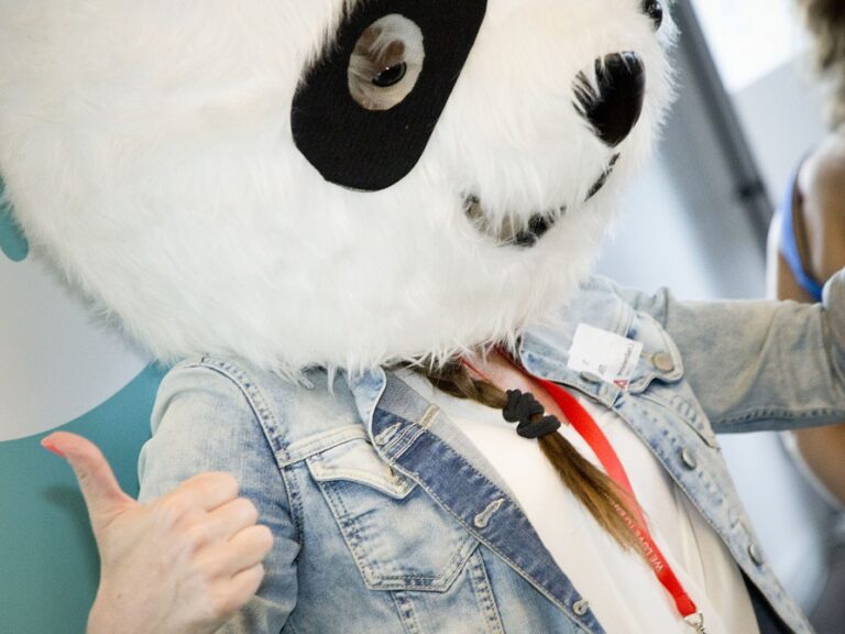 Photo of a woman with a braid wearing a costume Panda head, showing a thumbs up, at a PANDA Network event.